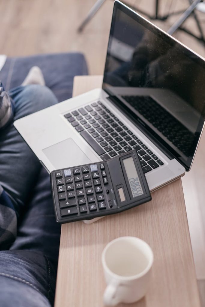 High angle view of a laptop and calculator on a wooden desk with a coffee mug.